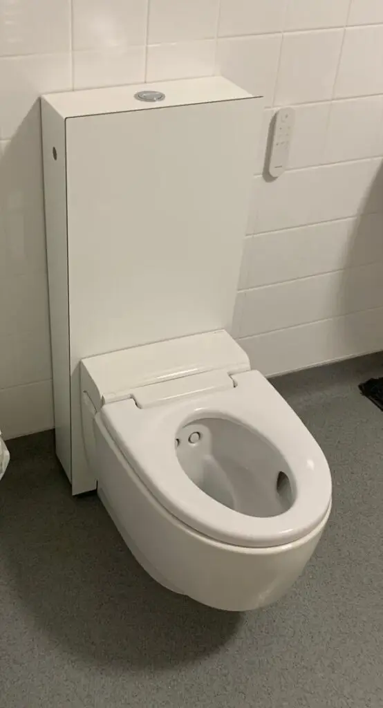 Modern white toilet with an electronic bidet seat installed against a white tiled wall.